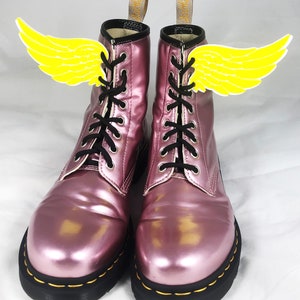 May include: A pair of pink metallic lace-up boots with yellow wings attached to the laces.