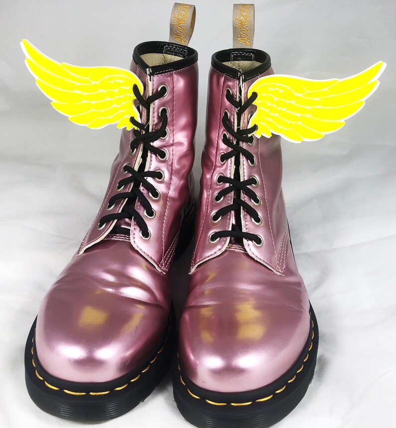 May include: A pair of pink metallic lace-up boots with yellow wings attached to the laces.