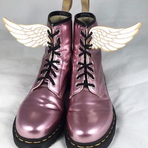 May include: Pink metallic leather lace-up boots with black laces and white wings attached to the sides.
