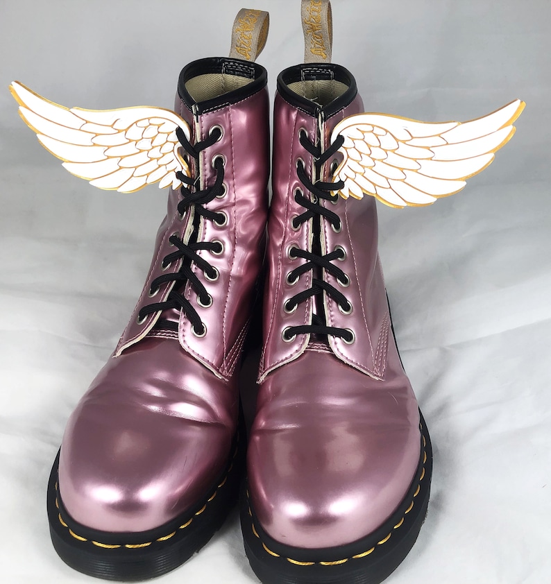 May include: Pink metallic leather lace-up boots with black laces and white wings attached to the sides.