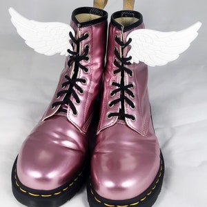 May include: A pair of pink patent leather lace-up boots with white angel wings attached to the laces.