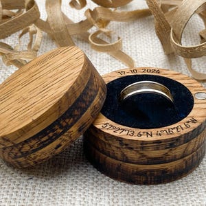 Peut inclure: Un &eacute;crin &agrave; bagues en bois avec une bague dor&eacute;e &agrave; l'int&eacute;rieur, sur fond neutre. La bo&icirc;te est ouverte, r&eacute;v&eacute;lant une bague nich&eacute;e dans un int&eacute;rieur en velours bleu fonc&eacute;. Le couvercle est &agrave; c&ocirc;t&eacute; de la bo&icirc;te. La date "19-10-2024" et des coordonn&eacute;es sont grav&eacute;es.