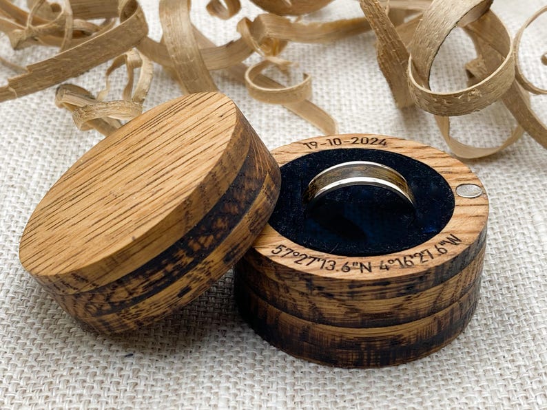 Peut inclure: Un &eacute;crin &agrave; bagues en bois avec une bague dor&eacute;e &agrave; l'int&eacute;rieur, sur fond neutre. La bo&icirc;te est ouverte, r&eacute;v&eacute;lant une bague nich&eacute;e dans un int&eacute;rieur en velours bleu fonc&eacute;. Le couvercle est &agrave; c&ocirc;t&eacute; de la bo&icirc;te. La date "19-10-2024" et des coordonn&eacute;es sont grav&eacute;es.