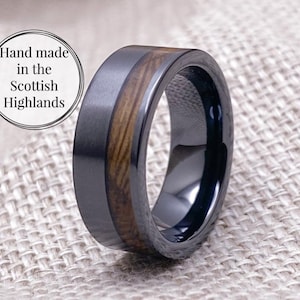 Puede incluir: Un anillo negro y marr&oacute;n con una incrustaci&oacute;n de madera. El anillo est&aacute; hecho de carburo de tungsteno y est&aacute; hecho a mano en las Highlands escocesas.
