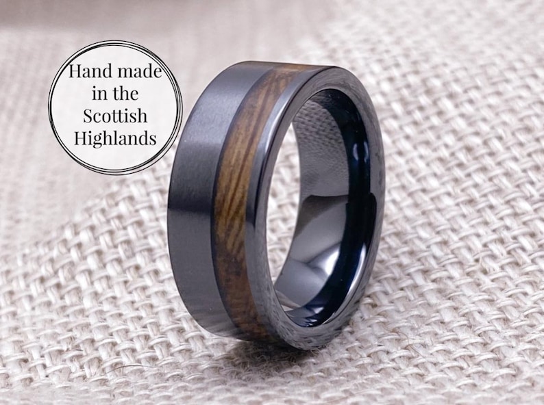 Puede incluir: Un anillo negro y marr&oacute;n con una incrustaci&oacute;n de madera. El anillo est&aacute; hecho de carburo de tungsteno y est&aacute; hecho a mano en las Highlands escocesas.