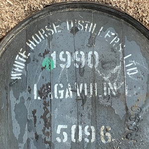 Puede incluir: Primer plano de un barril de madera gris con letras blancas. El barril est&aacute; etiquetado con "White Horse Distillers Ltd." y "1990".