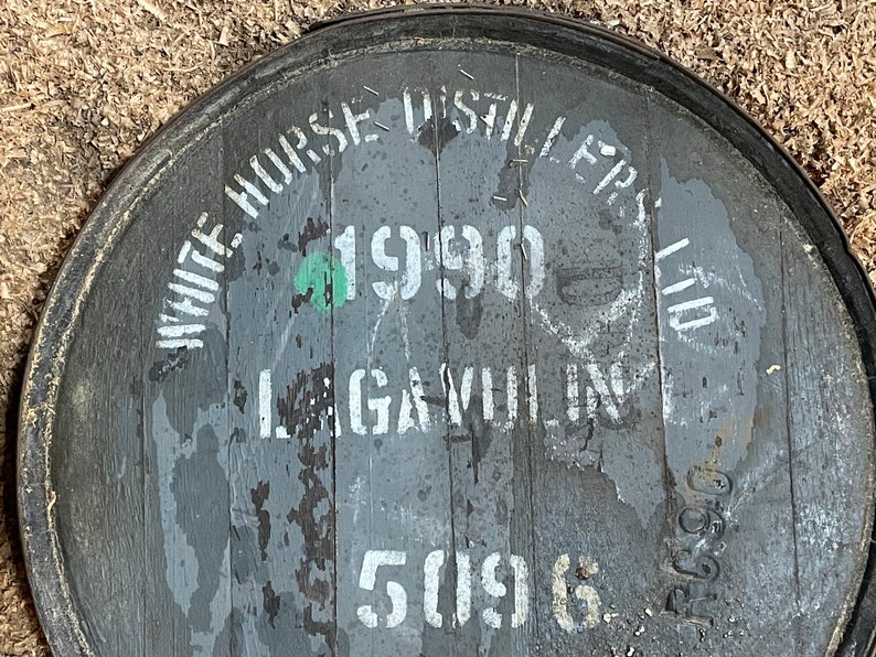 Puede incluir: Primer plano de un barril de madera gris con letras blancas. El barril est&aacute; etiquetado con "White Horse Distillers Ltd." y "1990".