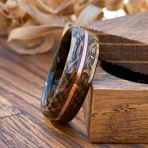 Whisky barrel wedding ring using Lagavulin whisky barrel cask with a centred copper highlight leaning on a oak ring box