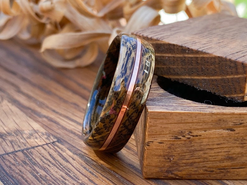 Whisky barrel wedding ring using Lagavulin whisky barrel cask with a centred copper highlight leaning on a oak ring box