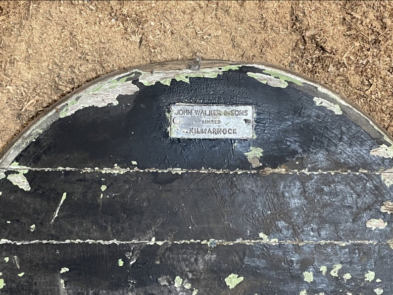 May include: A close-up of a black wooden surface with a silver metal plaque that reads "John Walker & Sons Limited - Kilmarnock".