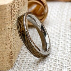 Peut inclure: Gros plan sur une bague avec un incrustation en bois et un anneau argent&eacute;. Le bois pr&eacute;sente un motif ray&eacute; dans des tons bruns et beiges. La bague est pos&eacute;e sur un fond neutre.