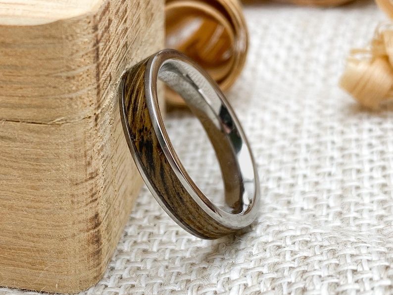Peut inclure: Gros plan sur une bague avec un incrustation en bois et un anneau argent&eacute;. Le bois pr&eacute;sente un motif ray&eacute; dans des tons bruns et beiges. La bague est pos&eacute;e sur un fond neutre.