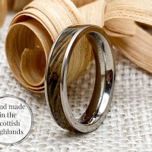 Peut inclure: Gros plan d'une bague argent&eacute;e avec incrustation de bois. La bague est mise en valeur sur un fond de copeaux de bois et une surface textur&eacute;e. Le texte "Hand made in the Scottish Highlands" est dans un cercle.