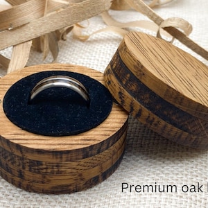 Peut inclure: Une bague argent&eacute;e avec une bande sombre est pr&eacute;sent&eacute;e dans un coffret rond en bois ouvert avec un int&eacute;rieur en velours noir. Le coffret en ch&ecirc;ne a une fermeture magn&eacute;tique. Le texte "Premium oak box" est visible.