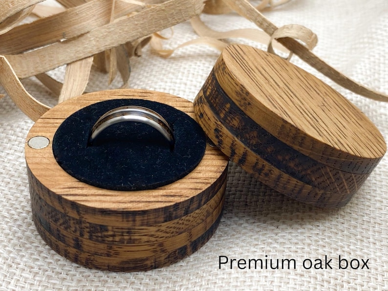Peut inclure: Une bague argent&eacute;e avec une bande sombre est pr&eacute;sent&eacute;e dans un coffret rond en bois ouvert avec un int&eacute;rieur en velours noir. Le coffret en ch&ecirc;ne a une fermeture magn&eacute;tique. Le texte "Premium oak box" est visible.