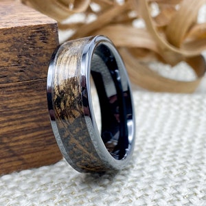 8mm black titanium carbide core with whisky distillery oak inlay of your choice, leaning on an oak ring box.