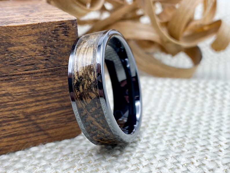 8mm black titanium carbide core with whisky distillery oak inlay of your choice, leaning on an oak ring box.