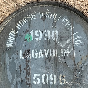 May include: Close-up of a gray wooden barrel with white lettering. The barrel is labeled "White Horse Distillers Ltd." and "1990".