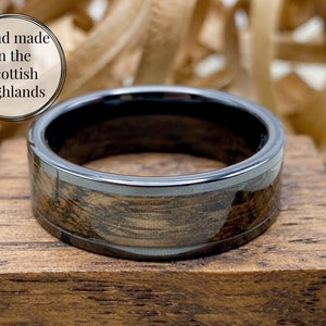 8mm black titanium carbide core with whisky distillery oak inlay of your choice, sitting flat on top of an oak ring box.