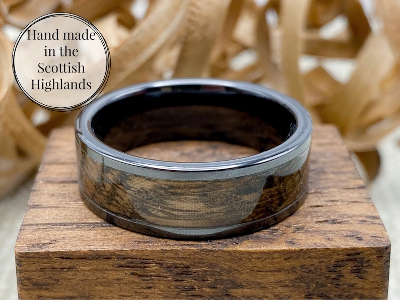 8mm black titanium carbide core with whisky distillery oak inlay of your choice, sitting flat on top of an oak ring box.