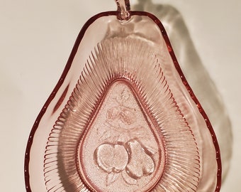 May include: A pink glass pear-shaped bowl with a ruffled edge. The bowl has a raised design of a pear with two apples inside.
