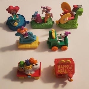 Puede incluir: Una colección de diez juguetes de Happy Meal con personajes de La Sirenita de Disney, Looney Tunes y Peanuts. Los juguetes están hechos de plástico y son de colores brillantes. Los juguetes incluyen a Ariel en una concha, Bugs Bunny en un cohete, el Pato Lucas en un piano, Snoopy en un caballito de balancín y una caja de Happy Meal con un personaje de dibujos animados.