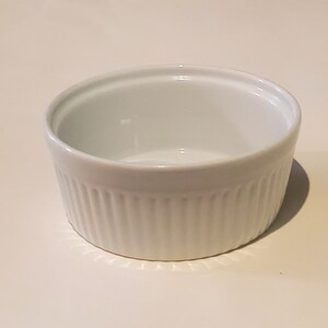 May include: A white ceramic ramekin with a fluted design. The ramekin is empty and ready to be used for baking or serving.