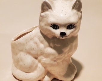 May include: White ceramic cat planter with speckled glaze. The cat is sitting with its head tilted down and has black eyes and a black nose.
