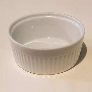 May include: White ceramic ramekin with a fluted design. The ramekin is empty and ready to be filled.
