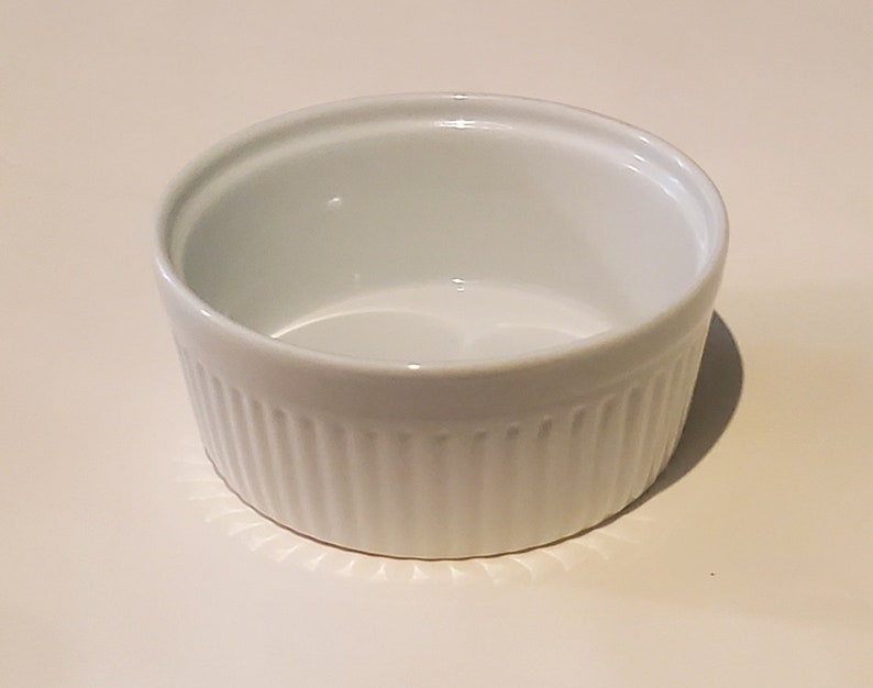 May include: White ceramic ramekin with a fluted design. The ramekin is empty and ready to be filled.