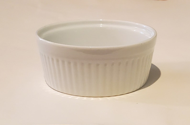 May include: White ceramic ramekin with a fluted design. The ramekin is empty and has a smooth, glossy finish.