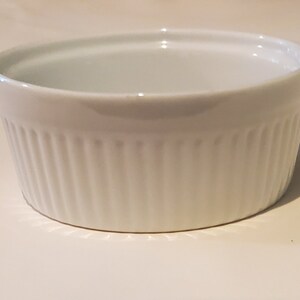 May include: White ceramic ramekin with a fluted design. The ramekin is empty and has a smooth, glossy finish.