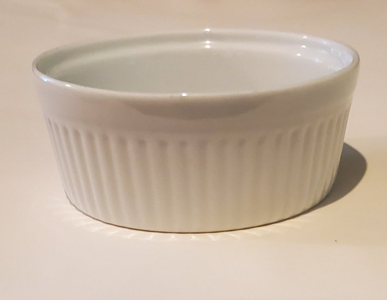 May include: White ceramic ramekin with a fluted design. The ramekin is empty and has a smooth, glossy finish.