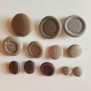 May include: Assortment of 12 brown and beige fabric buttons with a textured surface. The buttons are round and have a diameter of approximately 1 inch.