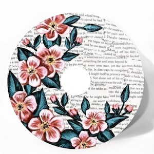 May include: A round sticker with a floral design featuring pink and white flowers with green leaves on a white background with text in the background.