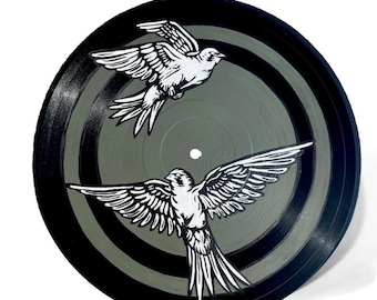 May include: A black vinyl record with a painted design featuring two white birds in flight. The record has a gray and black striped background. The birds are detailed with black outlines.