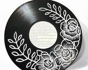 May include: A black vinyl record with white floral designs painted on the surface. The flowers are stylized and have a vintage look. The record is a circular shape and has a center hole.