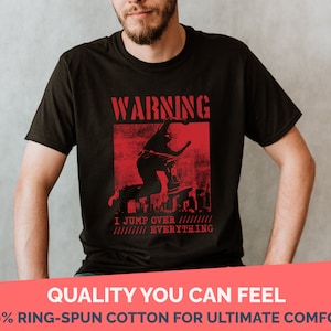 May include: Black t-shirt with a red graphic print of a person jumping over a city skyline. The graphic has the text "WARNING" and "I JUMP OVER EVERYTHING".