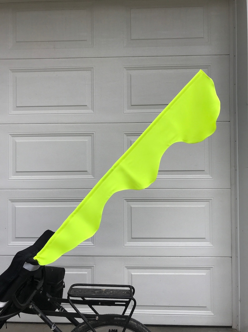 May include: A bright yellow safety flag attached to a bicycle. The flag is designed to increase visibility for cyclists on the road.