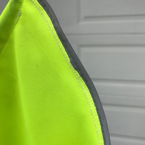 May include: Close-up of a bright yellow safety vest with a reflective gray trim. The vest is made of a durable fabric and has a sewn seam.