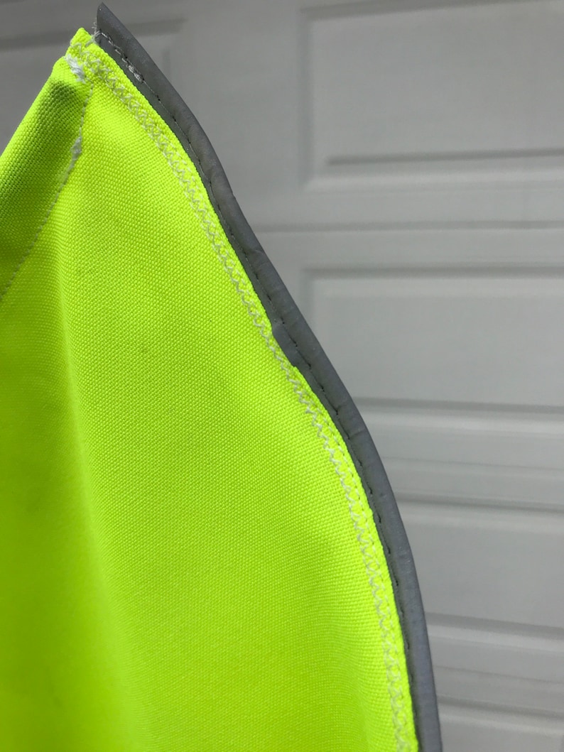 May include: Close-up of a bright yellow safety vest with a reflective gray trim. The vest is made of a durable fabric and has a sewn seam.