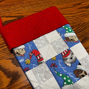 May include: A blue and white Christmas stocking with a red cuff. The stocking is decorated with a patchwork design featuring dogs wearing Santa hats and the words "ho ho ho".