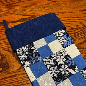 Può includere: Un calzino di Natale trapuntato blu e bianco con un motivo a fiocco di neve e un polsino in feltro blu.