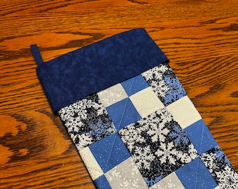 Pode incluir: Uma meia de Natal acolchoada azul e branca com um padrão de floco de neve e um punho de feltro azul.