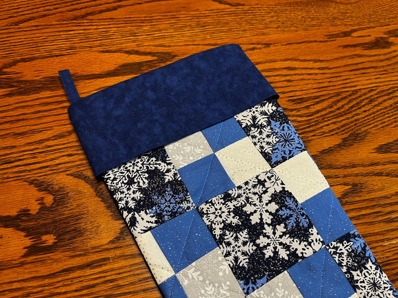 Puede incluir: Una media de Navidad acolchada azul y blanca con un patr&oacute;n de copo de nieve y un pu&ntilde;o de fieltro azul.