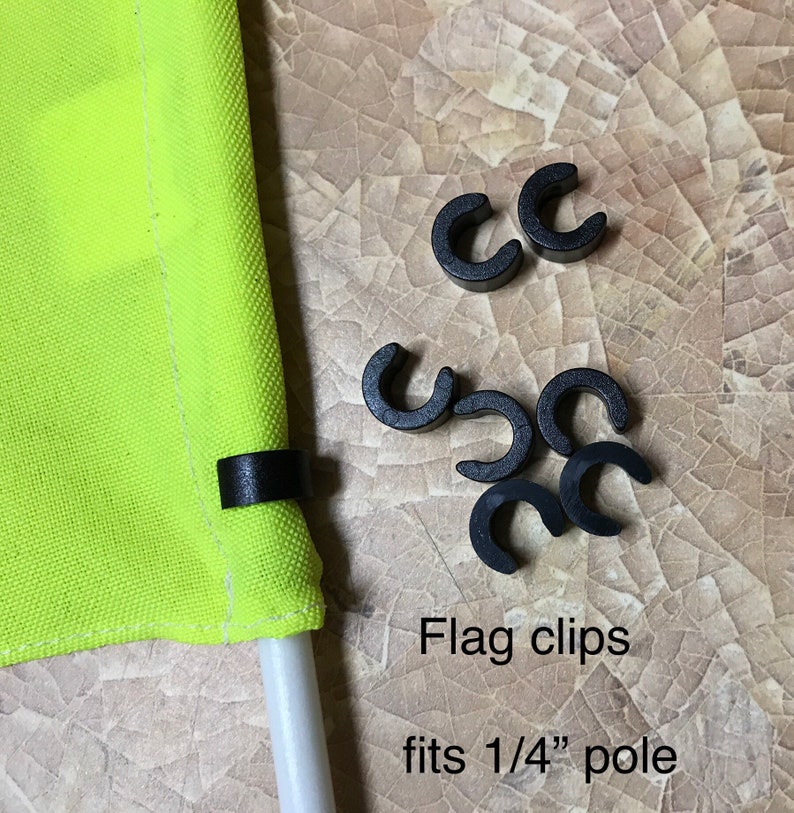 May include: Black plastic flag clips for a 1/4 inch pole. The clips are designed to hold a flag securely to a pole. The text "Flag clips fits 1/4" pole" is written below the clips.