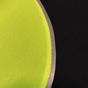 May include: Close-up of a bright yellow fabric with a reflective silver trim. The fabric is sewn with a white thread.