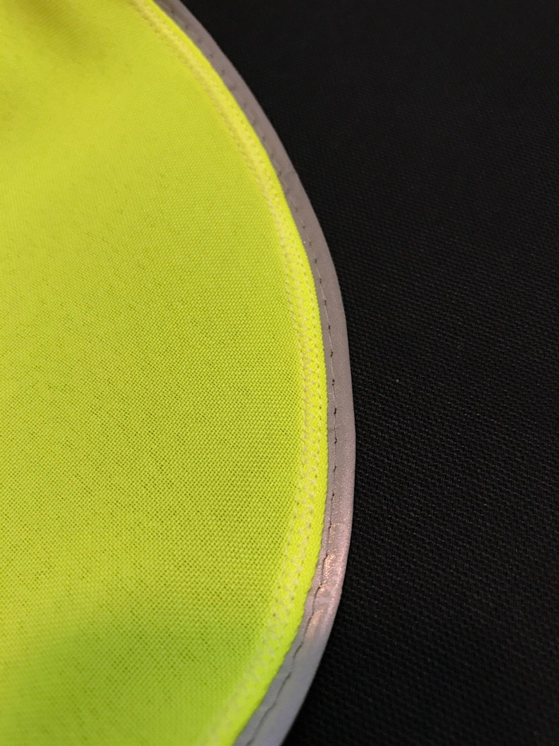 May include: Close-up of a bright yellow fabric with a reflective silver trim. The fabric is sewn with a white thread.