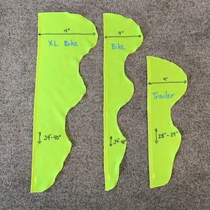 May include: Three yellow fabric pieces with measurements marked in inches. The largest piece is labeled "XL Bike" and measures 14 inches wide by 39-40 inches long. The middle piece is labeled "Bike" and measures 9 inches wide by 34-36 inches long. The smallest piece is labeled "Trailer" and measures 9 inches wide by 28-29 inches long.