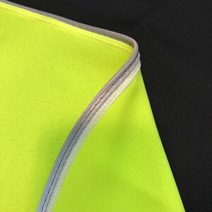 May include: Close-up of a bright yellow fabric with a reflective silver trim. The fabric is folded over and the trim is visible on the edge.